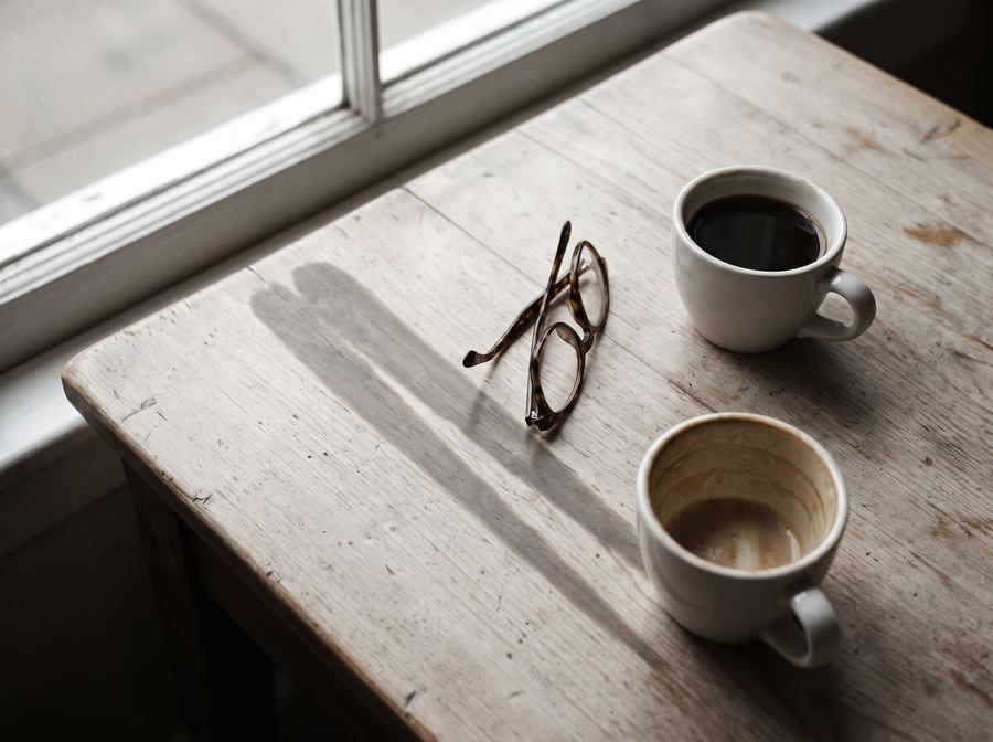 Duas xícaras de café sobre uma mesa de madeira, com um par de óculos entre elas