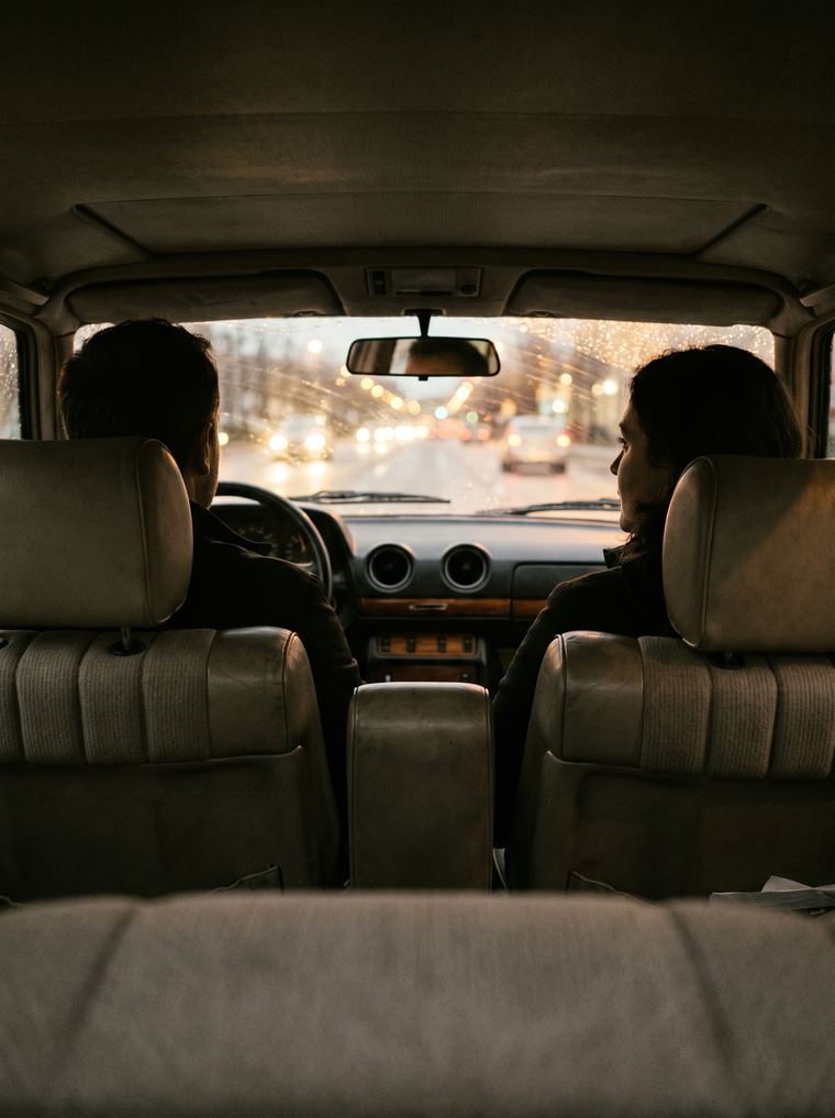 Interior de um carro ao entardecer, dois adultos em silhueta nos bancos da frente