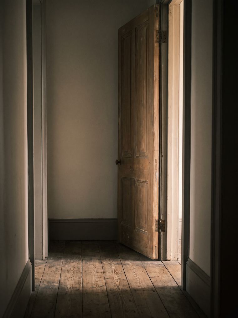 Corredor escuro com uma porta entreaberta e luz quente saindo pela fresta